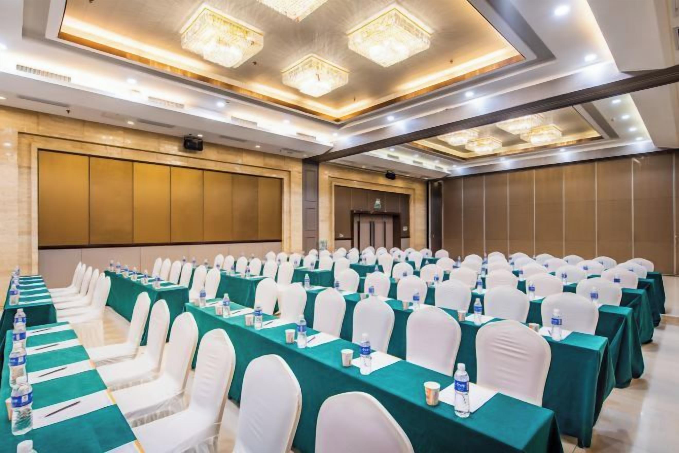 Un salón de conferencias con filas de mesas, sillas y una pantalla grande.