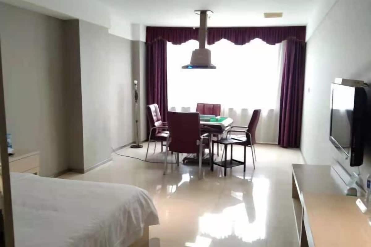A hotel room with a bed, a TV, a dining table with chairs, and a window with curtains.