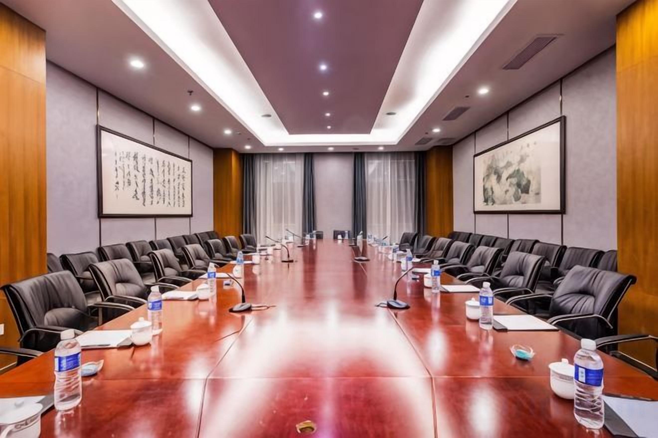 Un salón de conferencias con una larga mesa, sillas, micrófonos, botellas de agua y documentos.