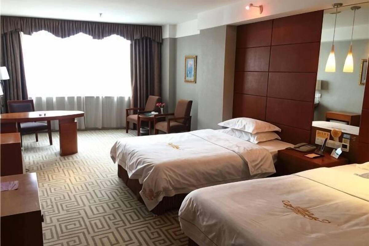A hotel room with two beds, a desk, a chair, a small table, and a window with curtains.