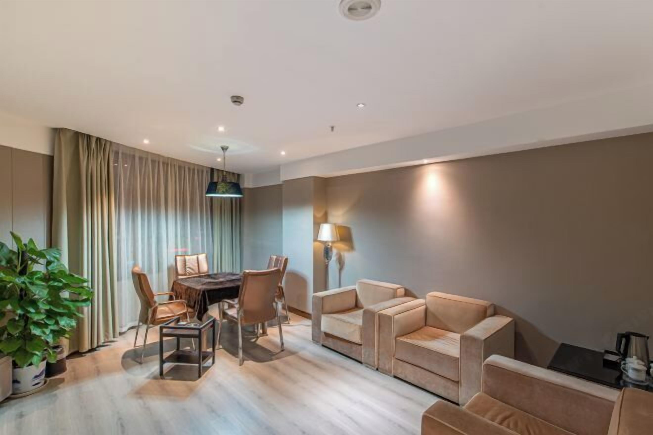 Una habitación de hotel moderna con zona de comedor, un conjunto de sofás y una planta en maceta.
