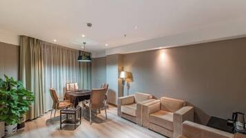 Una habitación de hotel moderna con zona de comedor, un conjunto de sofás y una planta en maceta.