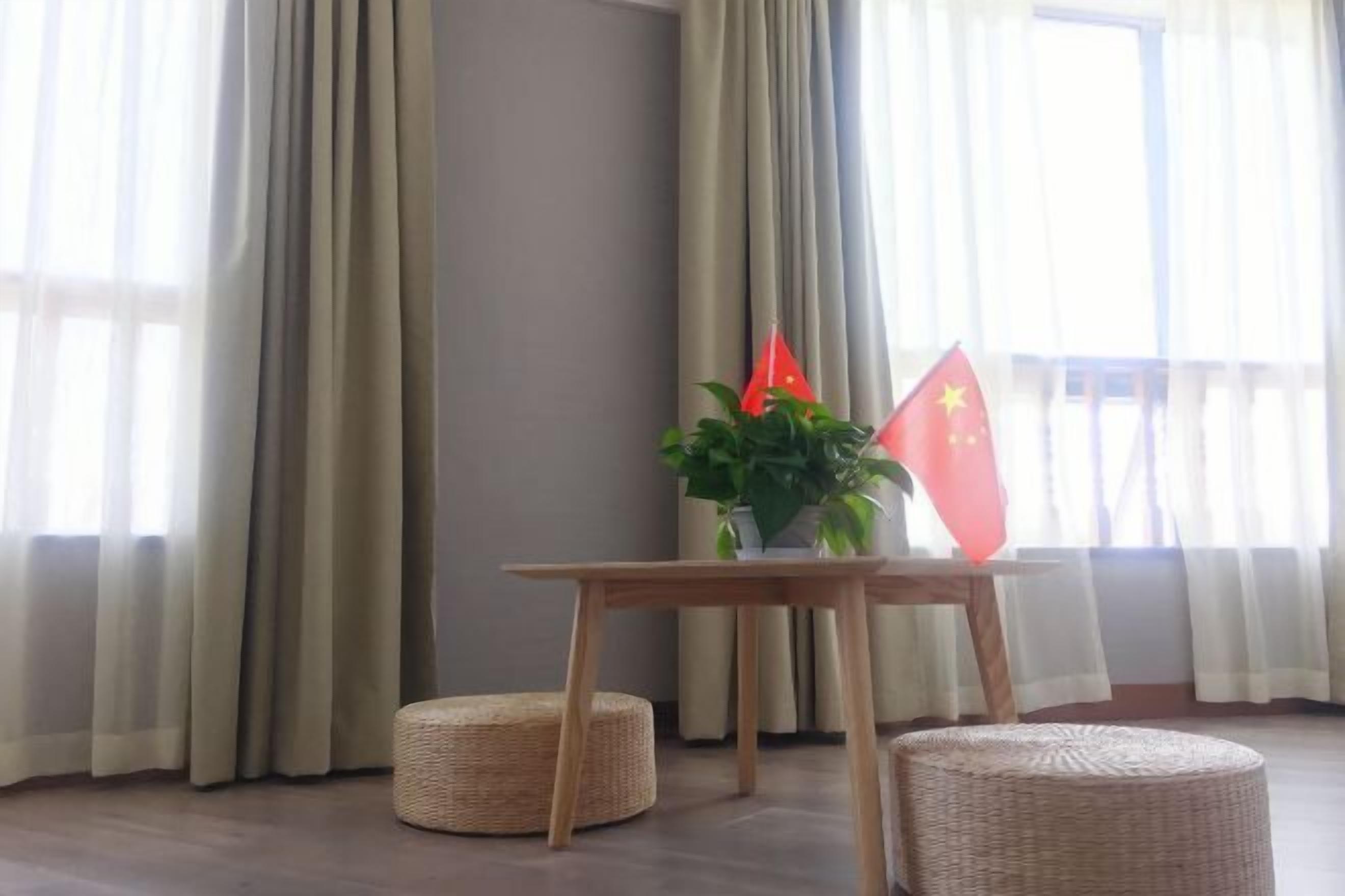 A room with a wooden table, two woven ottomans, a potted plant, and two flags.