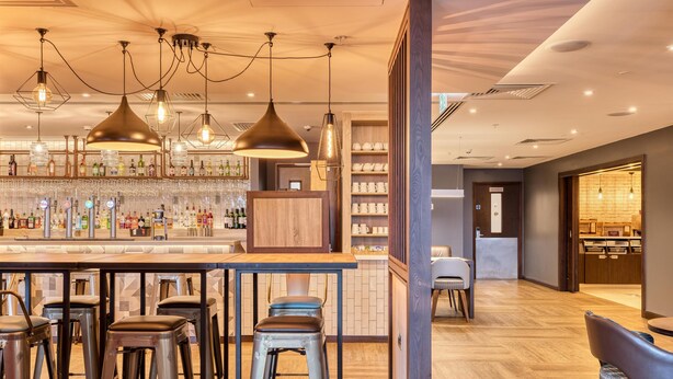 Un espace bar avec des tabourets, des suspensions lumineuses et un comptoir où sont exposées différentes bouteilles et différents verres.