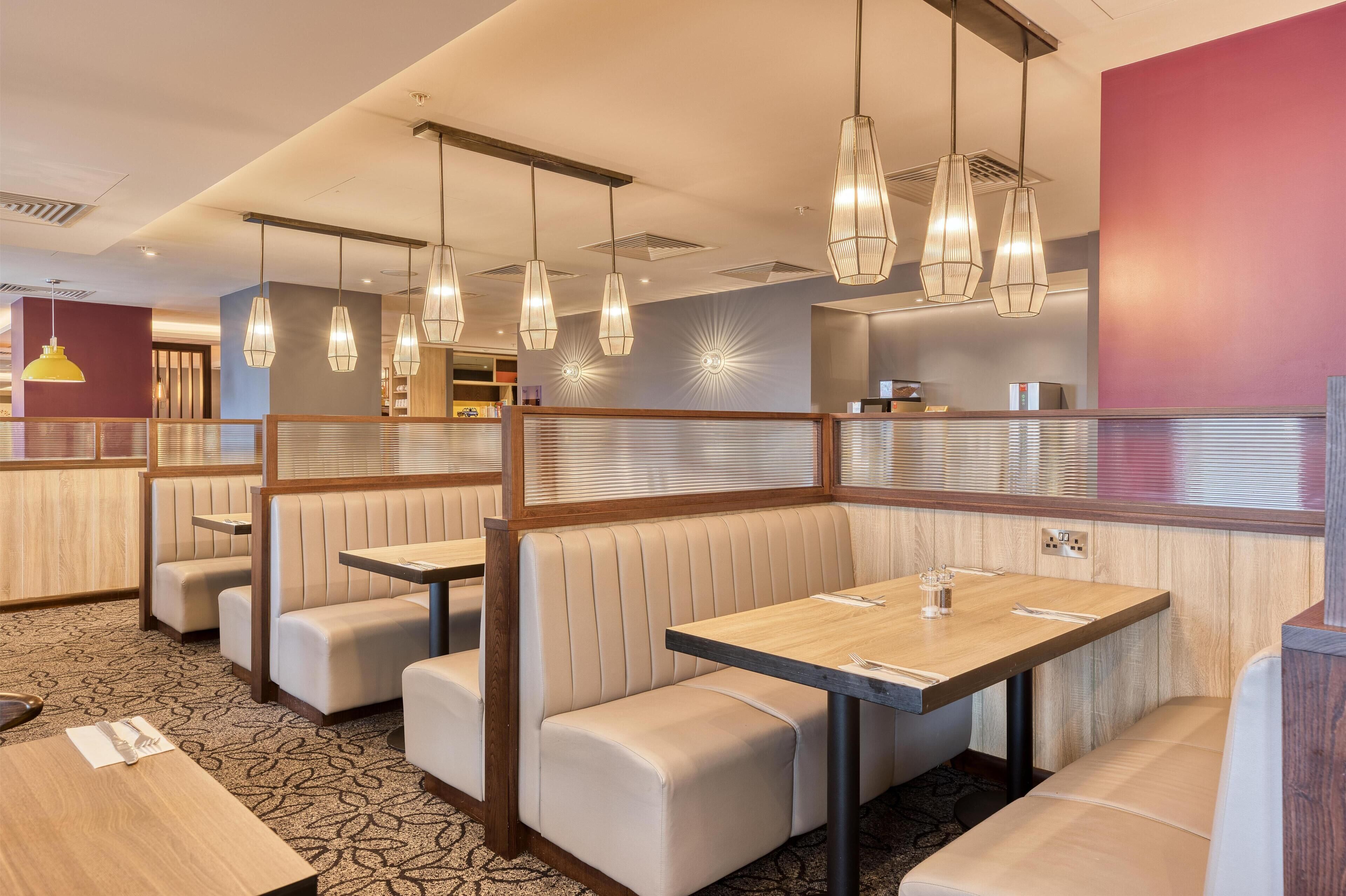 Un restaurante con cabinas y mesas, iluminación colgante y una alfombra estampada.