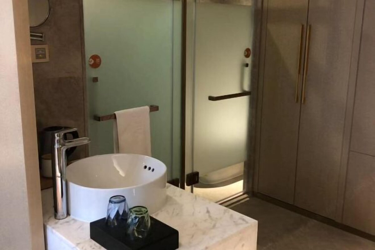 Ein Badezimmer mit einem weißen Waschbecken, einer Duschkabine aus Glas und einer Marmorarbeitsplatte.