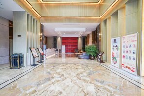 Un hall de hotel con piso de mármol, una recepción y una pared roja al fondo.