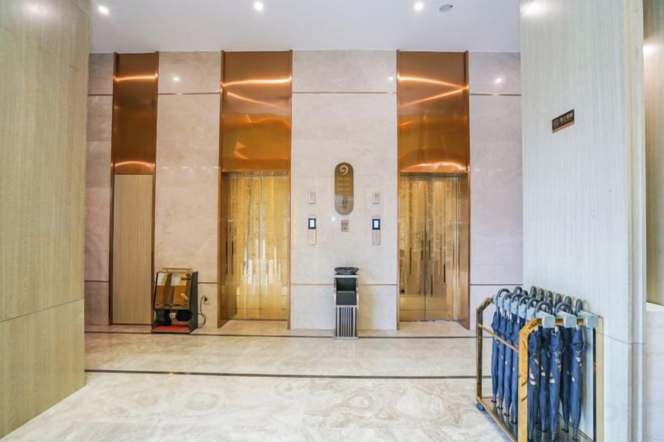 A hotel lobby with a marble floor, elevators, a reception desk, and a coat rack.