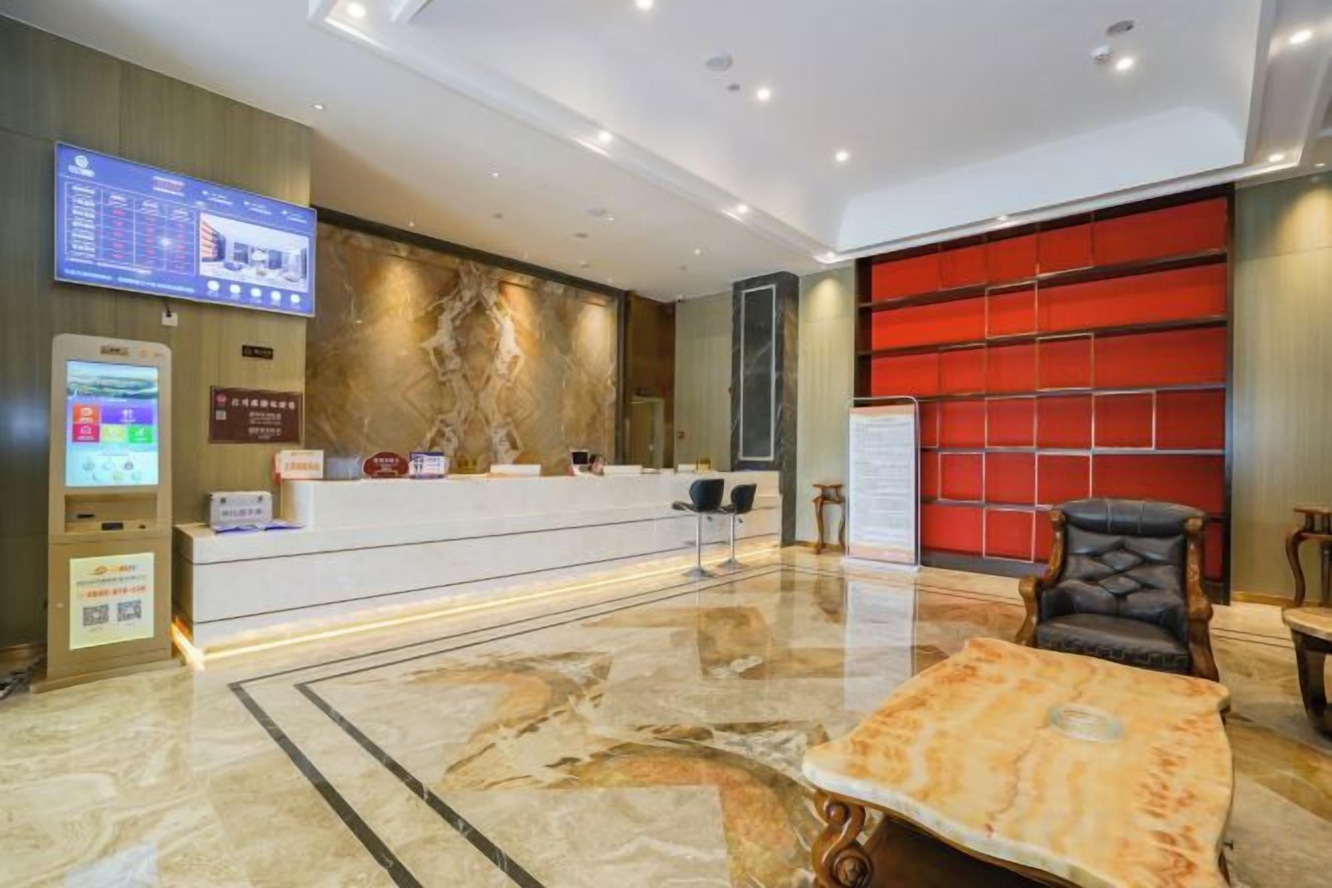 A hotel reception area with a marble floor, a reception desk, a digital screen, and a red wall.