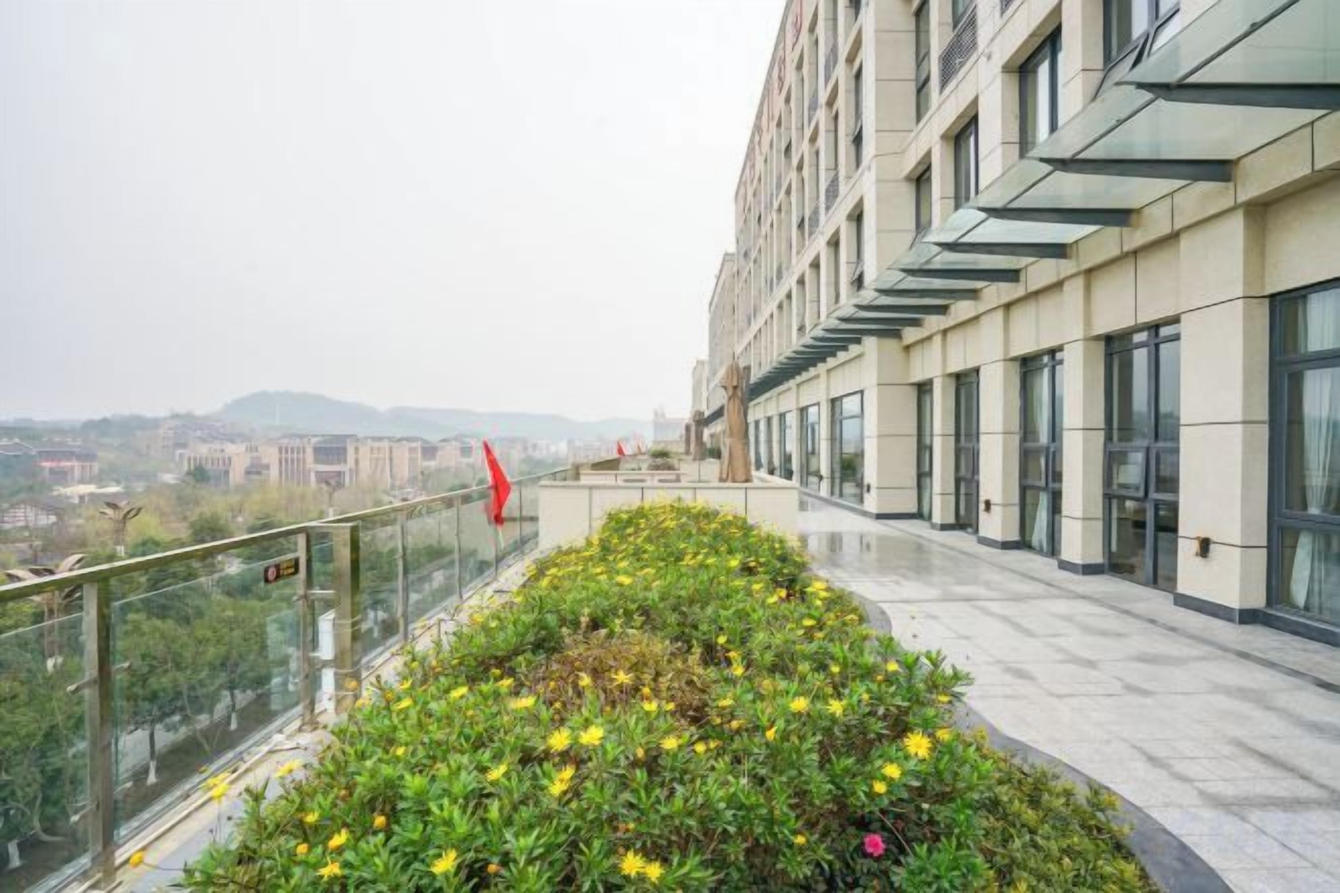 Un bâtiment moderne doté d’une façade en verre, d’un espace paysager agrémenté de fleurs et offrant une vue sur le paysage urbain.