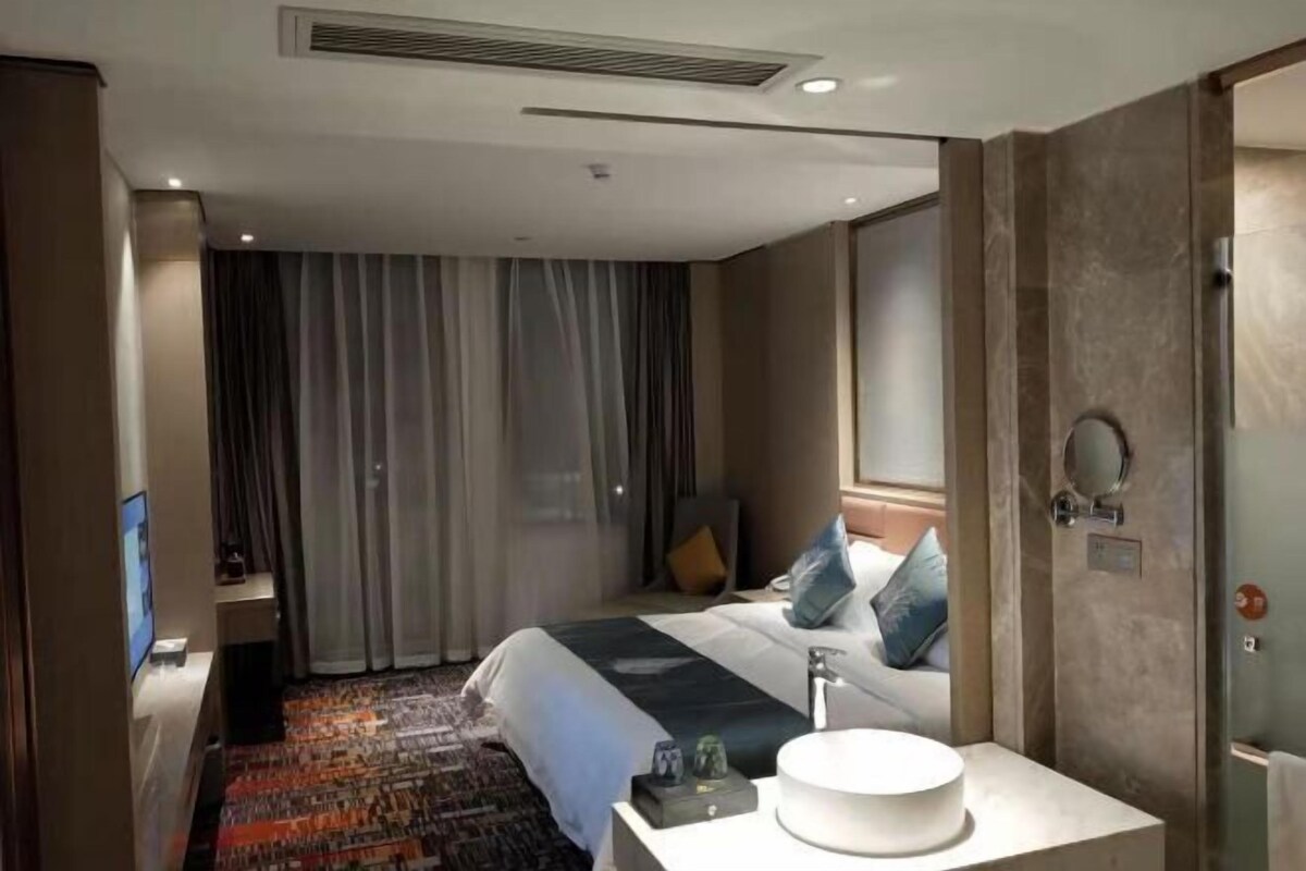 A hotel room with a bed, a bedside table with a lamp, a bathroom with a mirror, and a television.