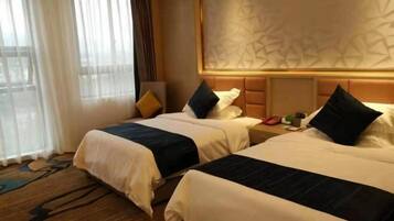 A hotel room with two beds, a large window with sheer curtains, a patterned wall, and a wooden floor.