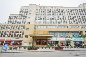 A multi-story hotel with a prominent entrance, several ground-level shops, and a parking area. - Mingwu Jiuzun Hotel (Mianyang)