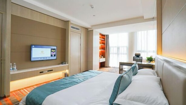 Une chambre d’hôtel avec un lit, un téléviseur fixé au mur, un bureau avec une chaise et une fenêtre avec des rideaux.