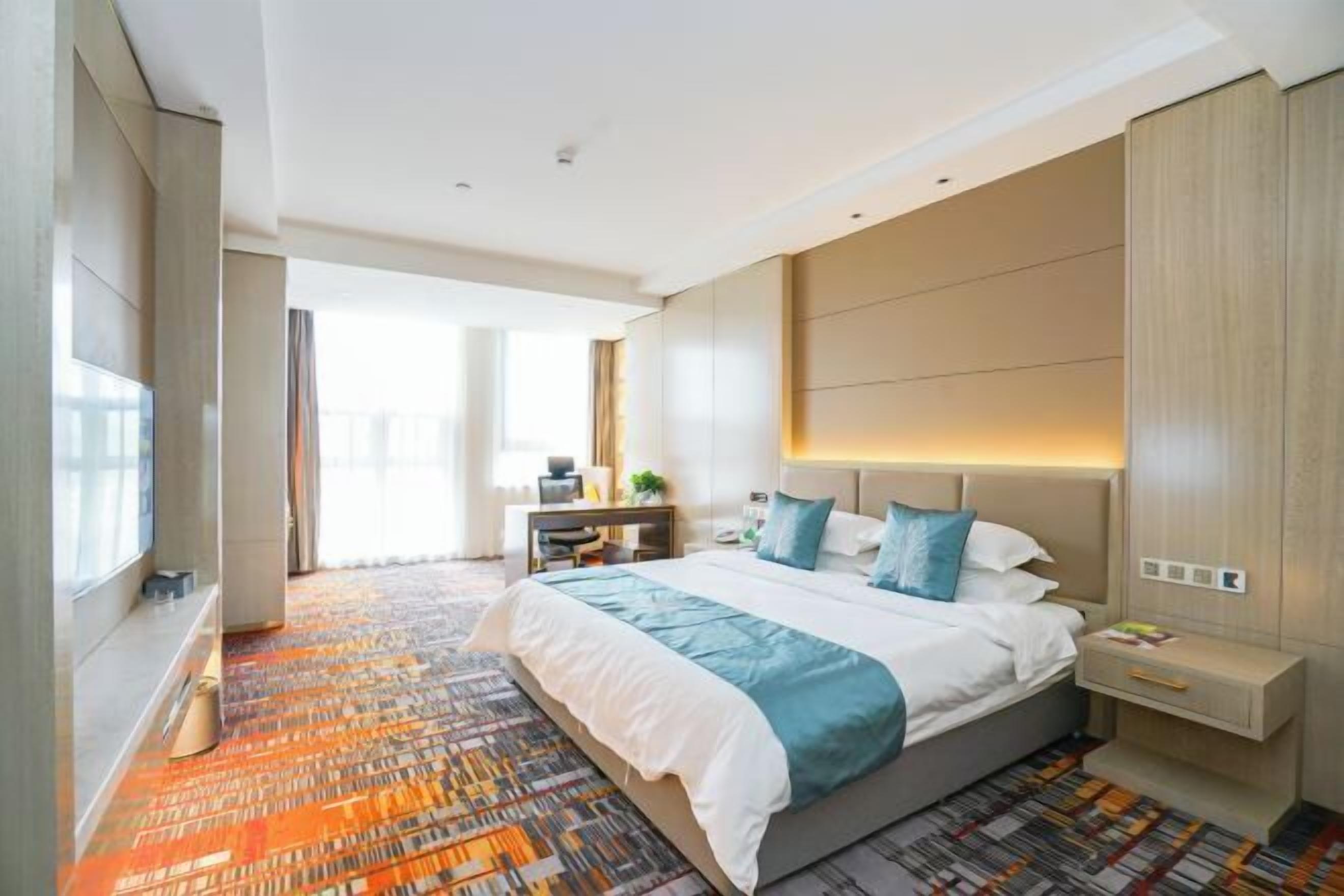 A modern hotel room with a large bed, a bedside table, a nightstand, and a view of the outdoors.