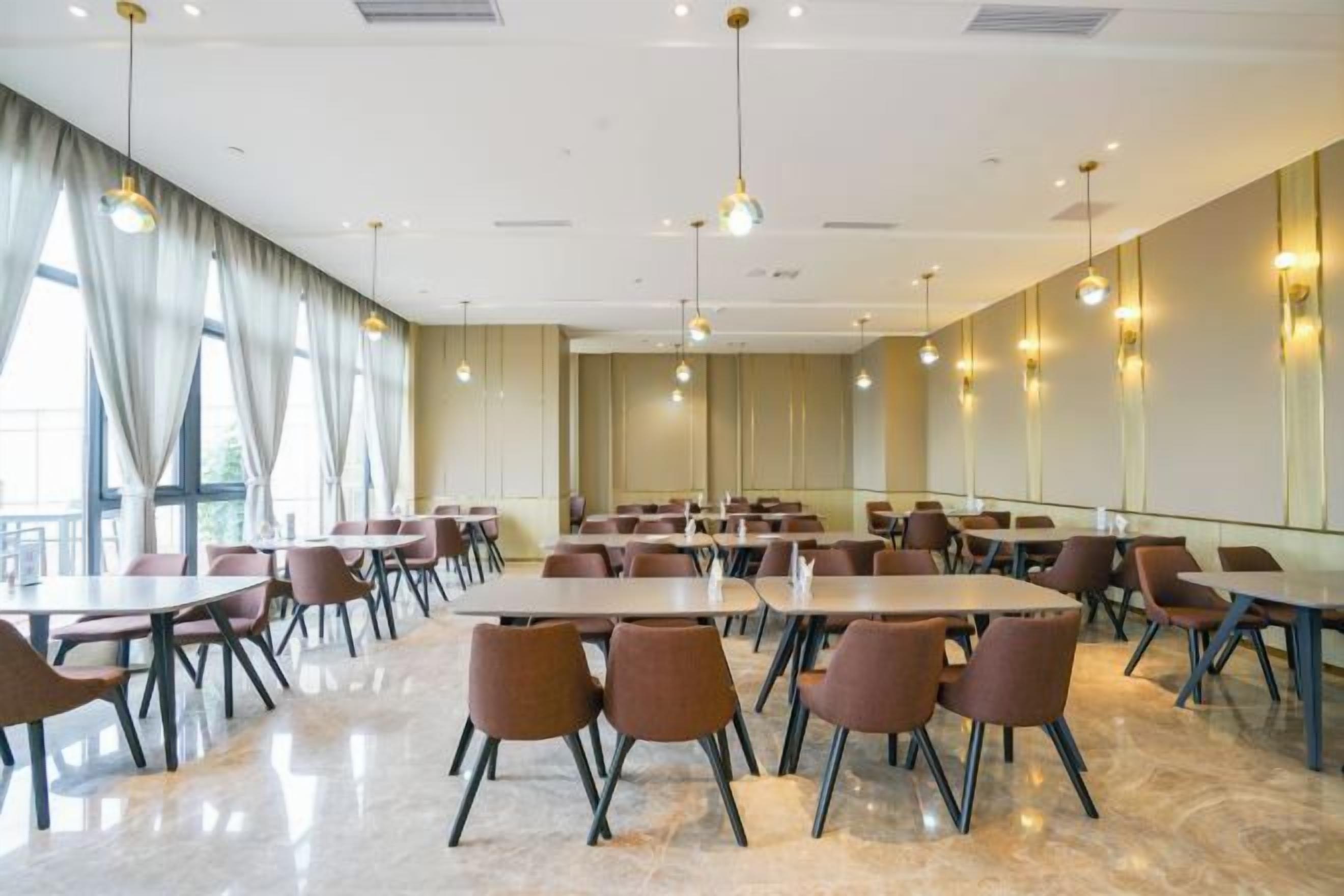 Une salle de conférence dotée de plusieurs tables et chaises, de grandes fenêtres avec des rideaux et d’un éclairage suspendu.