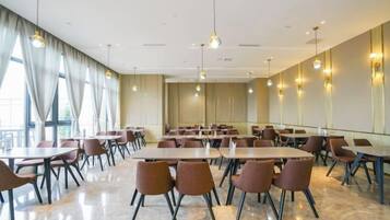 Une salle de conférence dotée de plusieurs tables et chaises, de grandes fenêtres avec des rideaux et d’un éclairage suspendu.