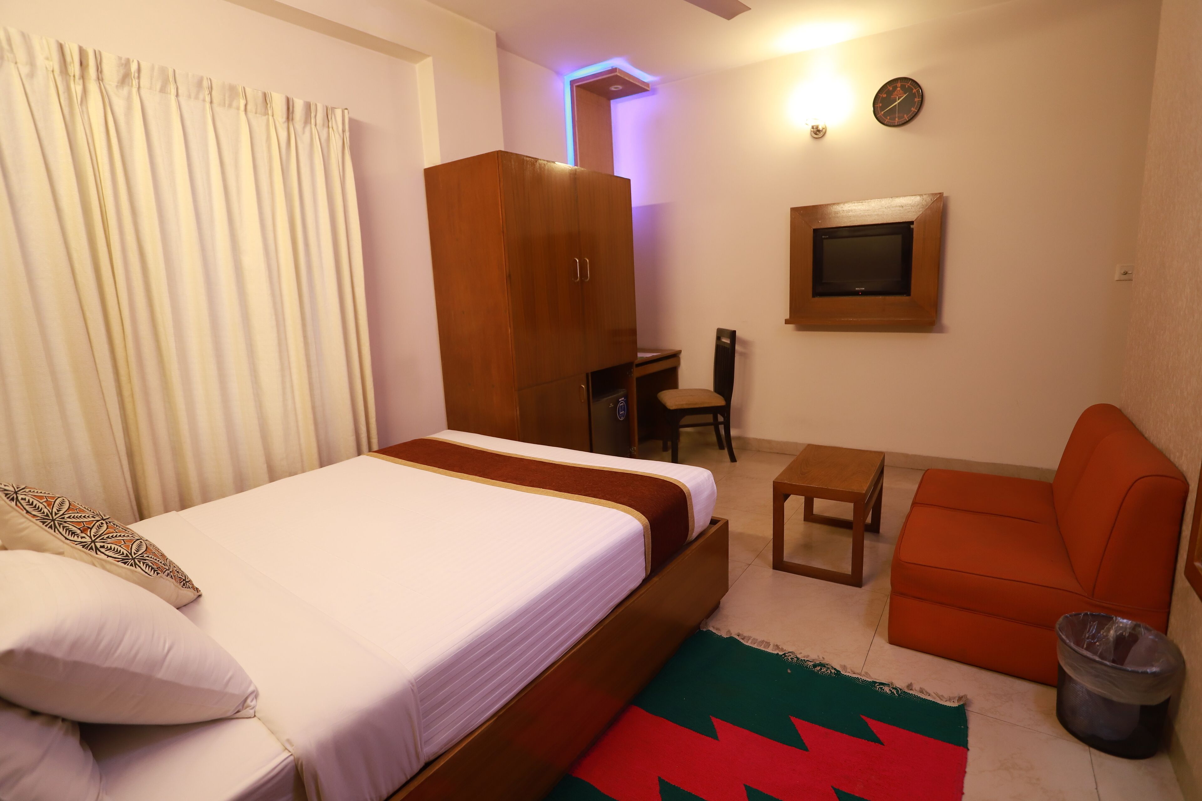 A hotel room with a bed, a desk, a chair, a television, and a wardrobe.