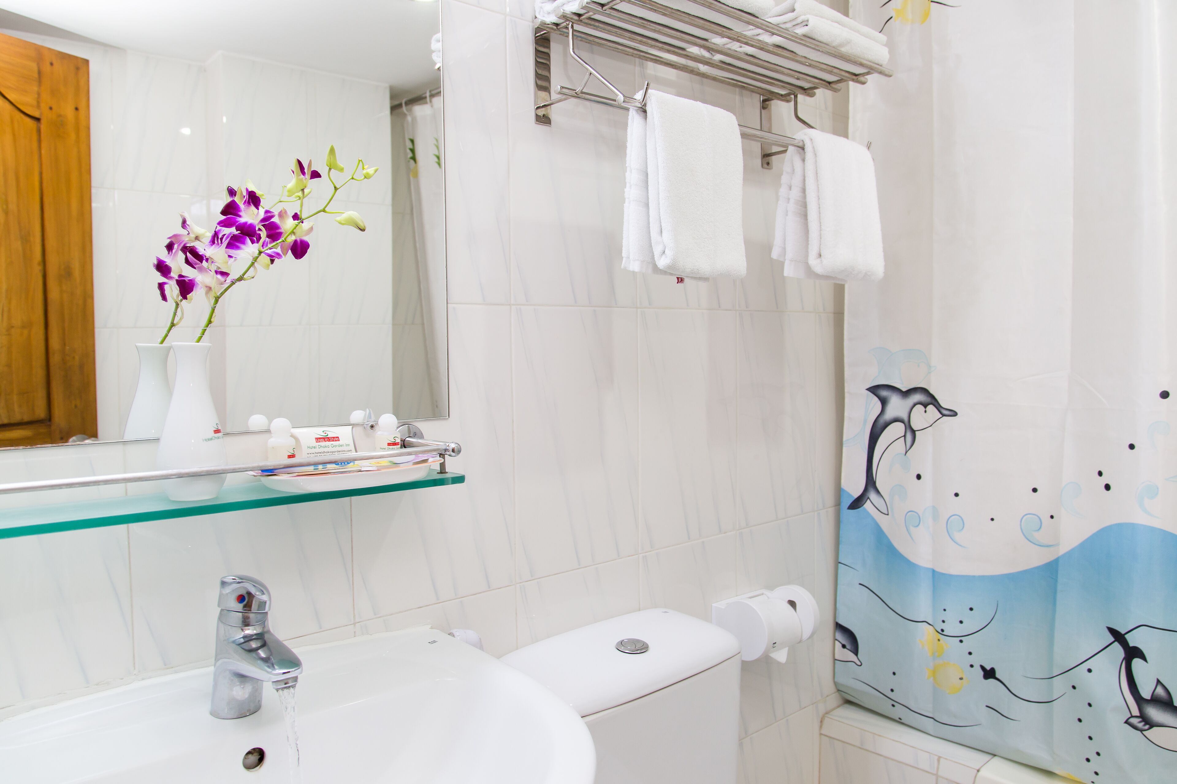 A bathroom with a white sink, a glass shelf with toiletries, a mirror, and a shower curtain with a dolphin design.