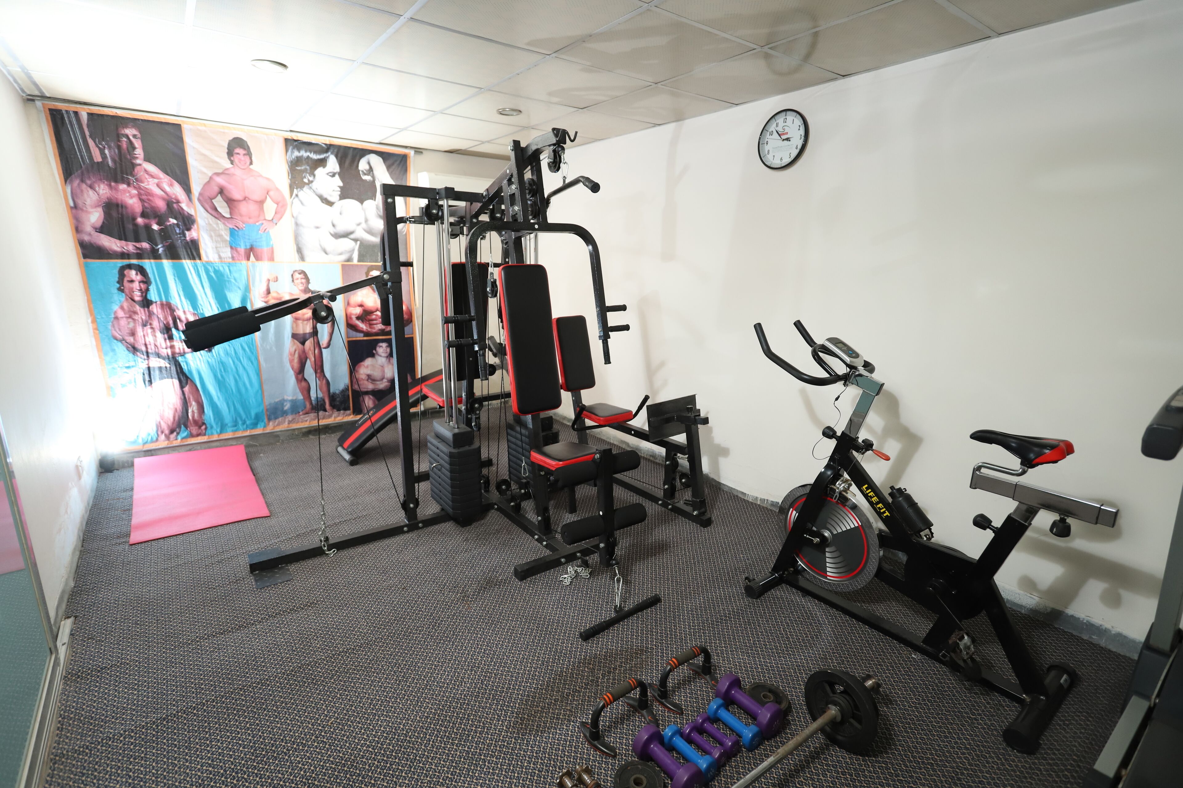 Uma academia com equipamentos de exercício, uma bicicleta ergométrica e um relógio na parede.