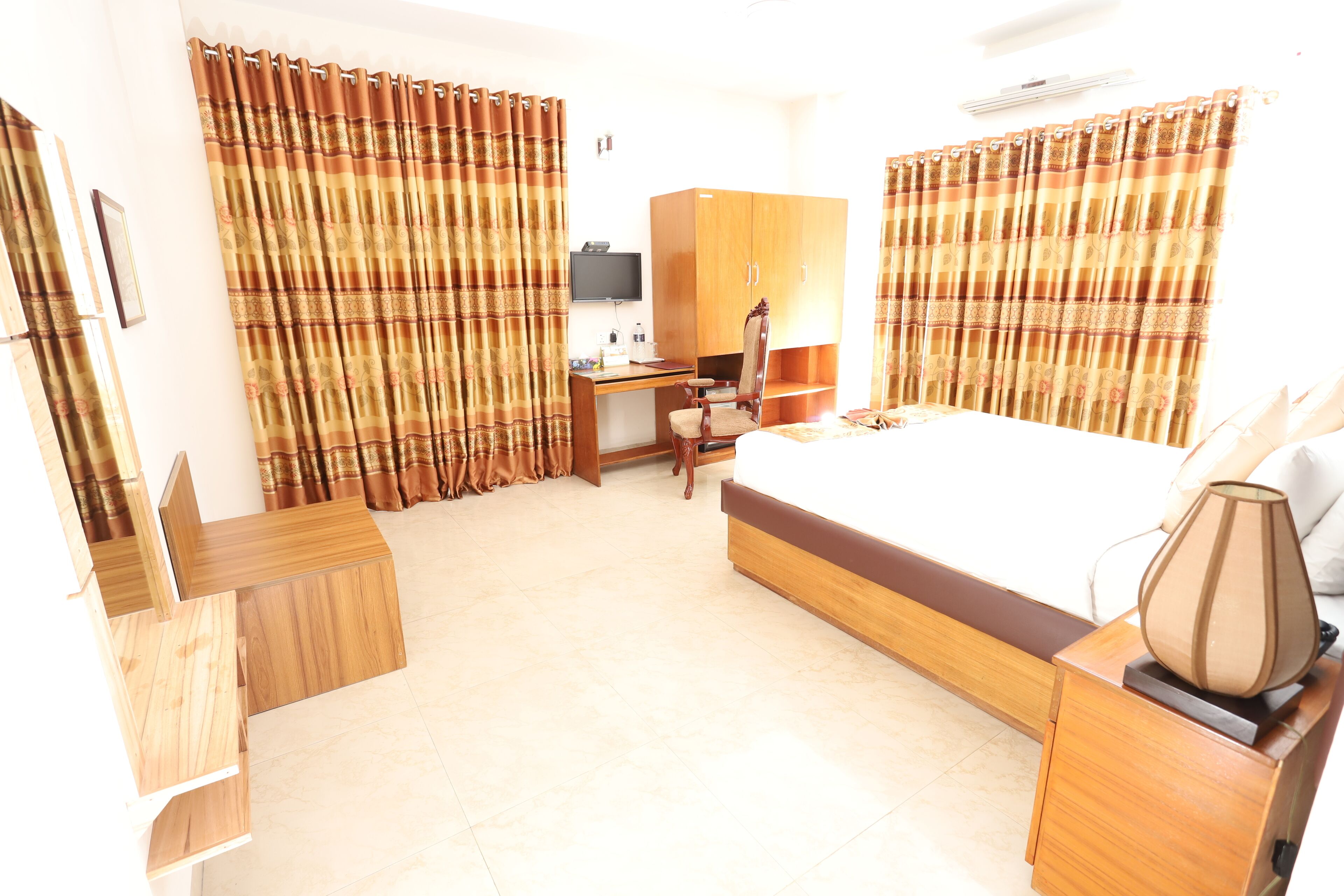 A hotel room with a bed, desk, wardrobe, and curtains.
