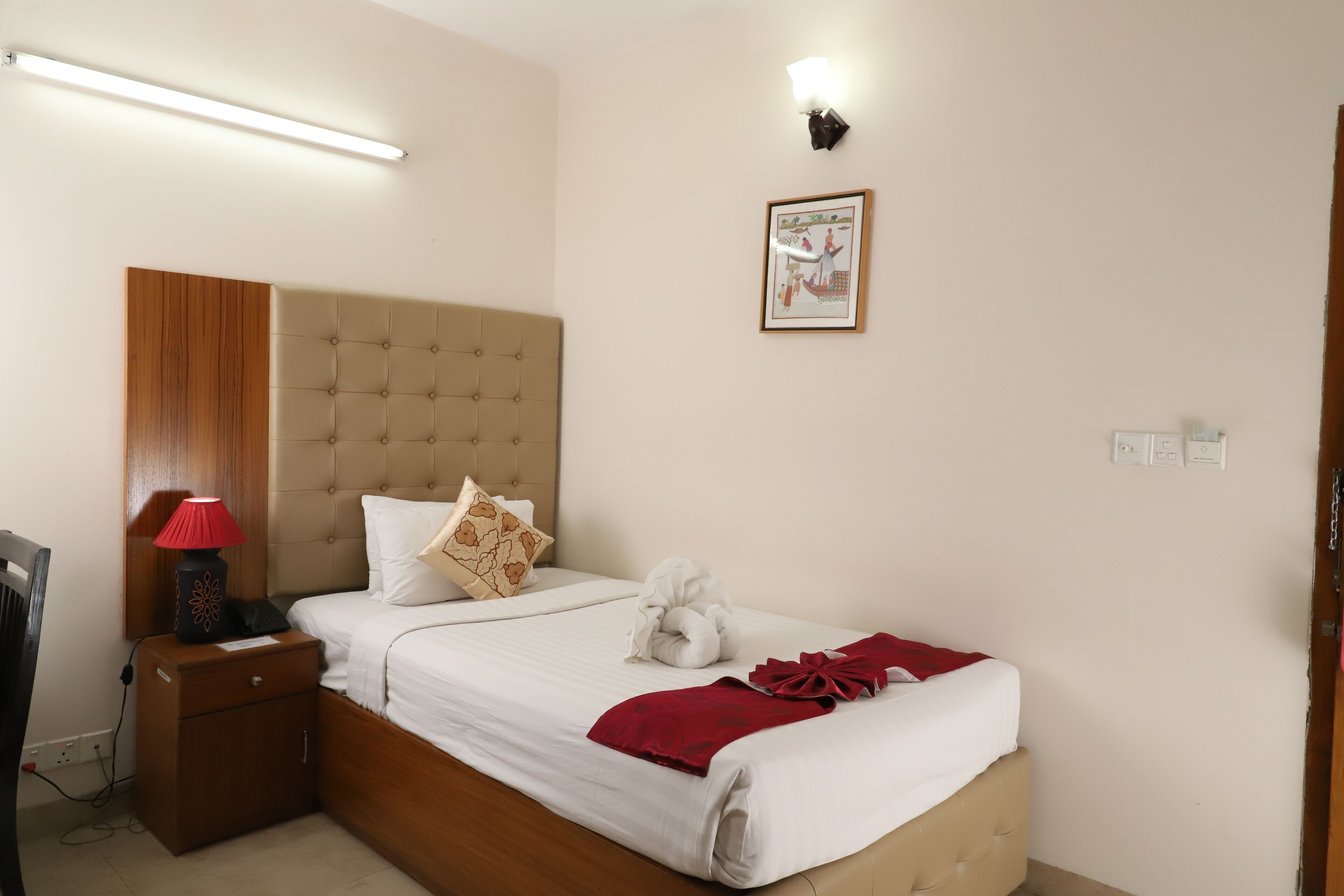 A neatly made bed with a red blanket, a bedside lamp, and a framed picture on the wall.