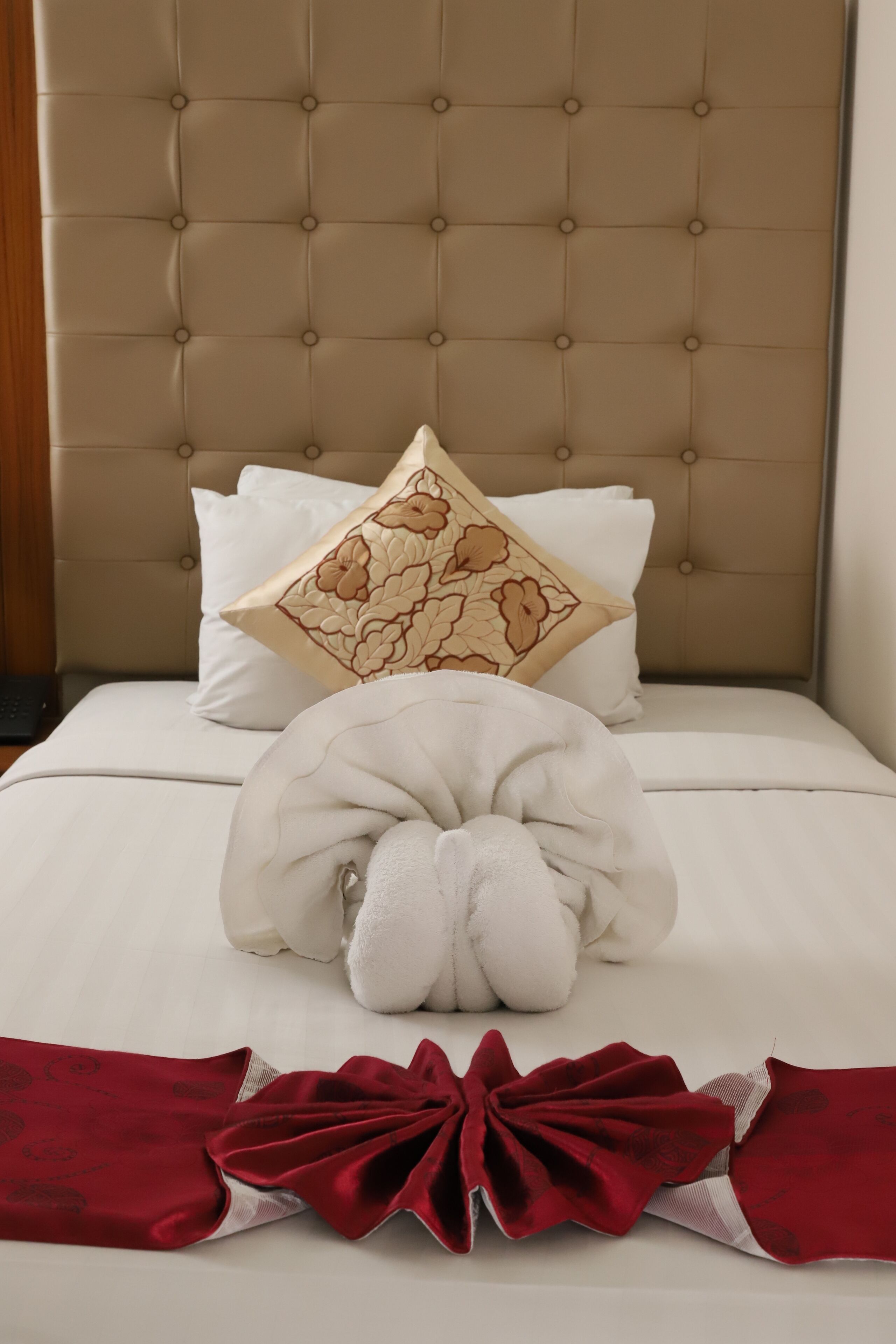 A neatly made bed with a tufted headboard, white pillows, and a decorative pillow with a floral pattern.