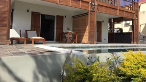 Ein Poolbereich mit Holzterrasse, überdachter Sitzgelegenheit und einer Steinmauer.