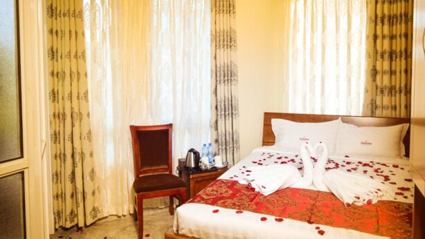 A hotel room with a bed, curtains, a chair, and a small table with a kettle and water bottles. - Velvet Hotel and Restaurant (Nairobi)