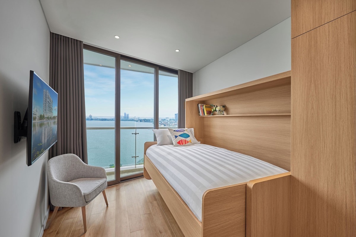 Quarto moderno com cama, uma cadeira, televisão e vista para a cidade.