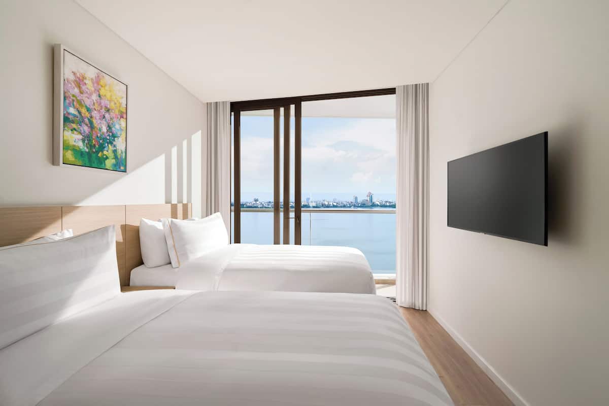 Une chambre d’hôtel avec un lit, un téléviseur à écran plat, un tableau et une vue sur la ville.