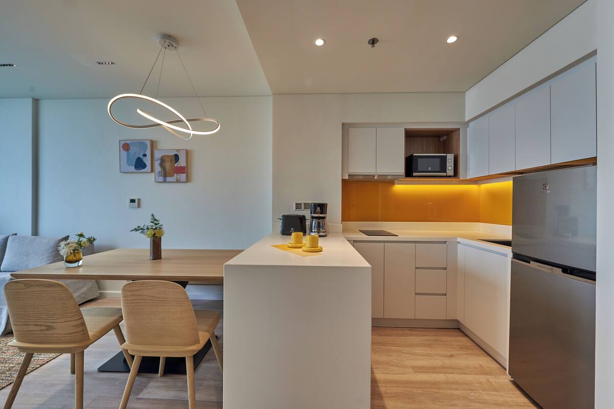 Una cocina moderna con una isla central, muebles blancos y un refrigerador de acero inoxidable.