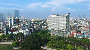 A modern hotel with a glass facade, surrounded by lush greenery and a river.