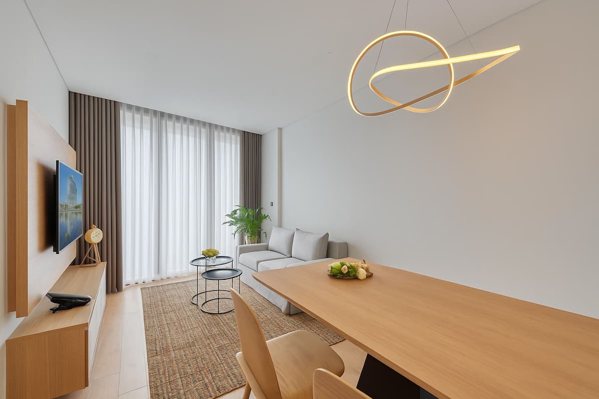 Una sala moderna con una mesa de comedor de madera, un sofá, un televisor y un ventanal con cortinas.