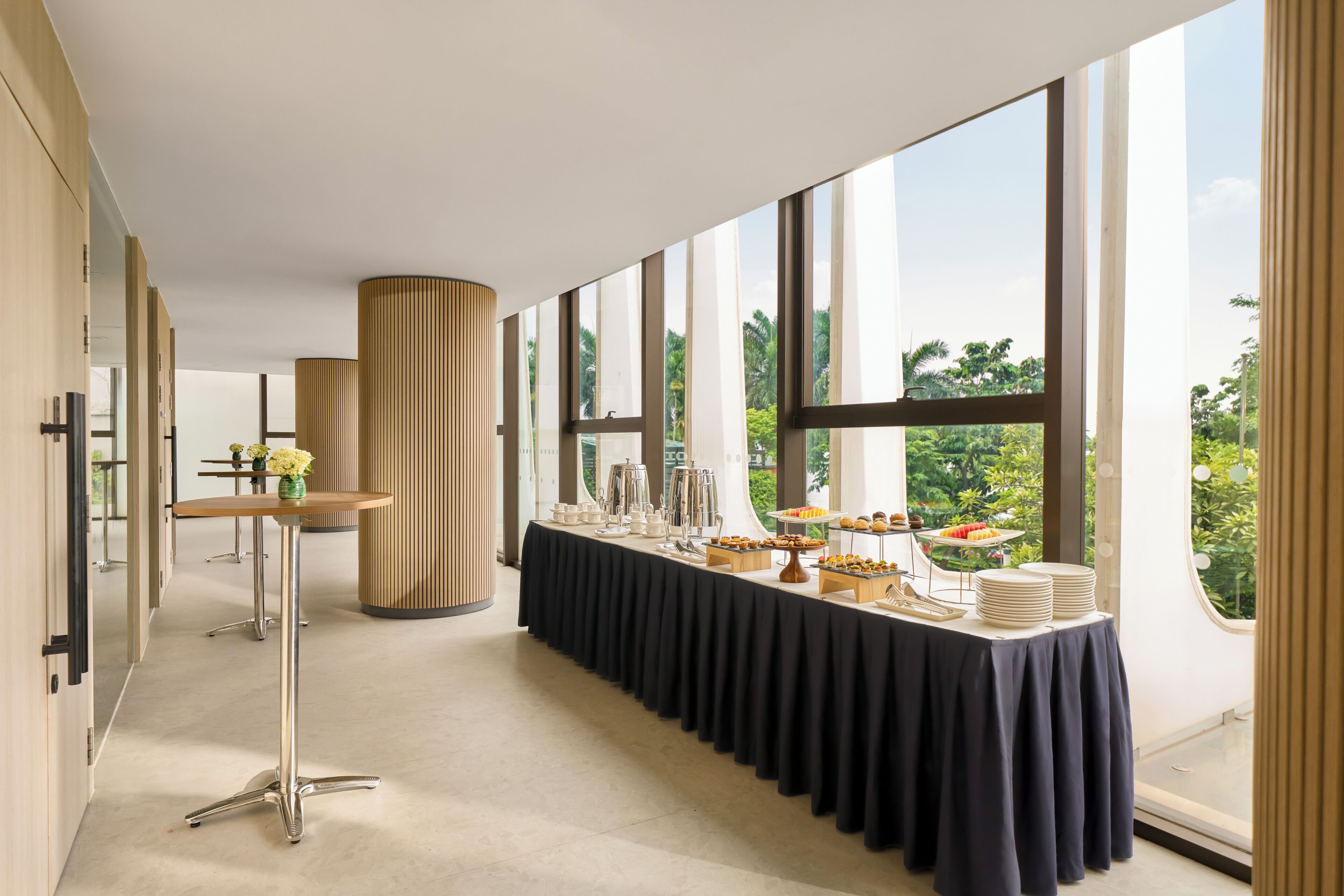 A long buffet table with various food items, set in a room with large windows and a modern interior design.