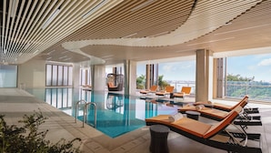 Un área de piscina interior moderna con sillones de descanso y vistas a la ciudad.