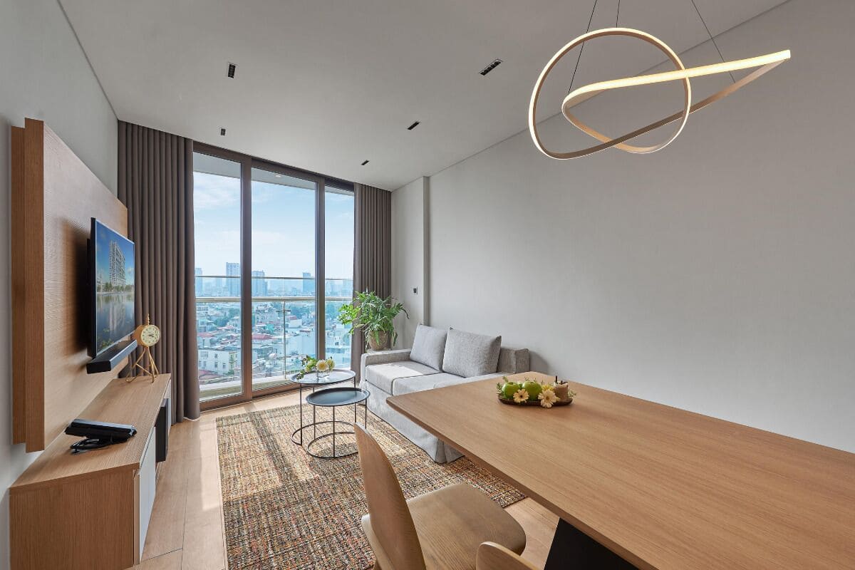 Una sala de estar moderna con una mesa de comedor de madera, un sofá, un televisor y un ventanal con vistas a la ciudad.