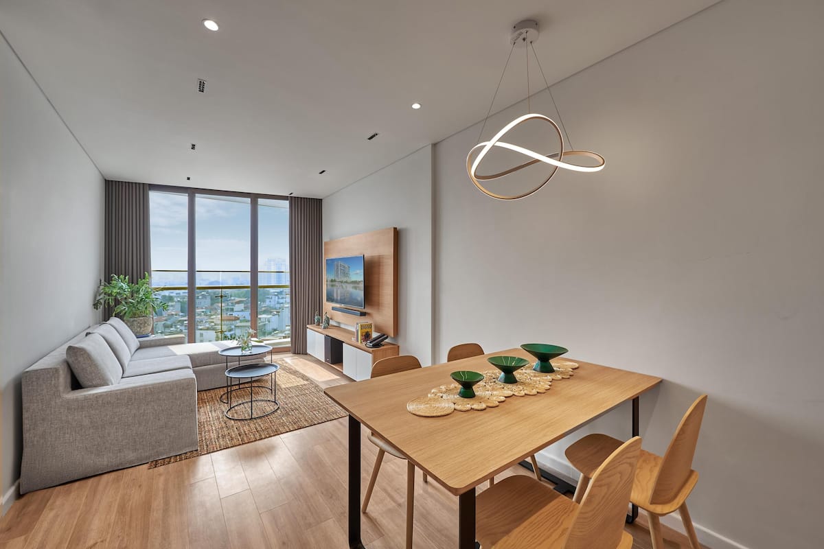 Una sala de estar moderna con un sofá, una mesa de comedor y sillas. Hay un televisor y una planta en la habitación.