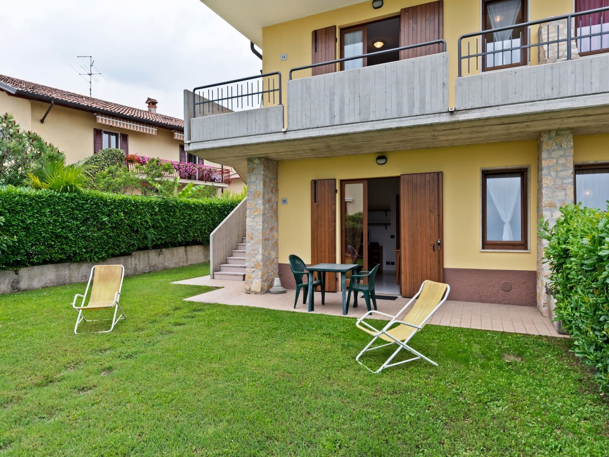 A two-story building with a balcony, a small patio with chairs, and a well-maintained lawn.