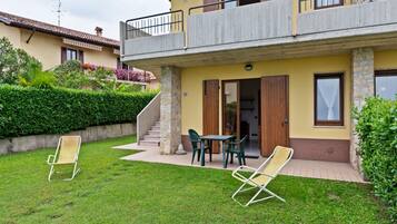 A two-story building with a balcony, a small patio with chairs, and a well-maintained lawn.