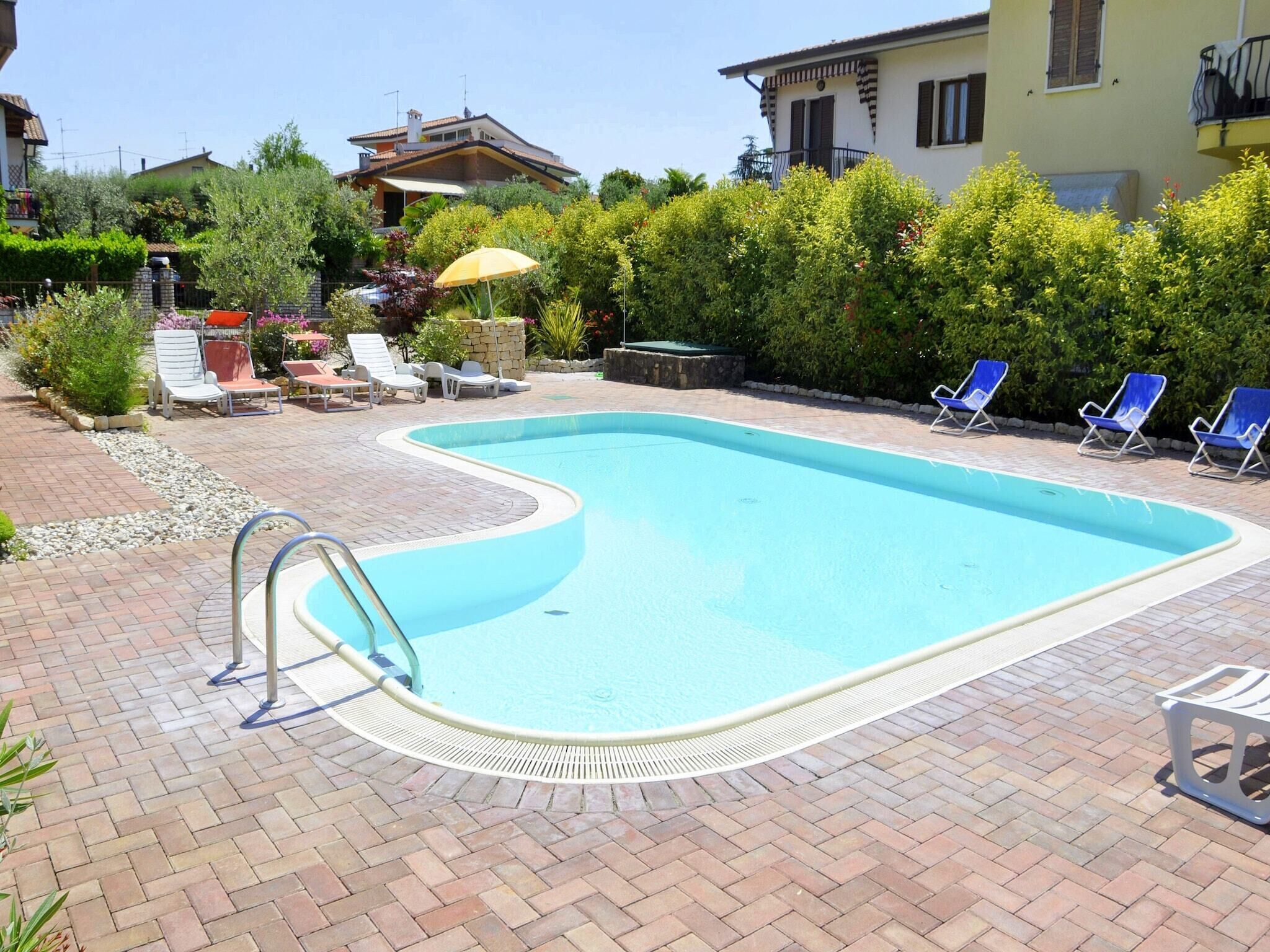 A swimming pool with a curved edge, surrounded by a brick patio, and adjacent to a house with a balcony.