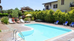Ein Schwimmbecken mit geschwungener Kante, umgeben von einer Ziegelterrasse, neben einem Haus mit Balkon.
