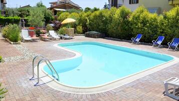 A swimming pool with a curved edge, surrounded by a brick patio, and adjacent to a house with a balcony.