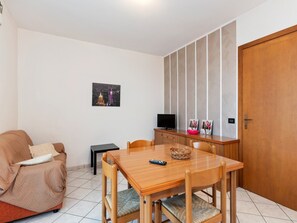 A small, cozy room with a wooden dining table, a sofa, a TV on a wooden cabinet, and a door. - Holiday Home in Lazise near Lake Garda (Lazise)