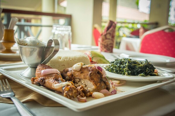 A dining table with a plate of food, including a piece of meat, greens, and a bowl of soup.