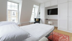 A bedroom with a bed, white walls, a TV, and a window.