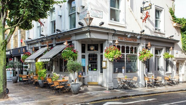 A corner building with "The Champion" signage, outdoor seating with tables and chairs, and hanging flower baskets.