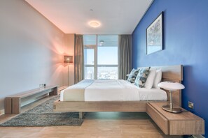 A modern bedroom with a large bed, a bedside table, a lamp, and a view of the city through a window. - Maison Privee - Skyline & Sea Vw Nxt to Beach, in Dubai Marina (Dubai)