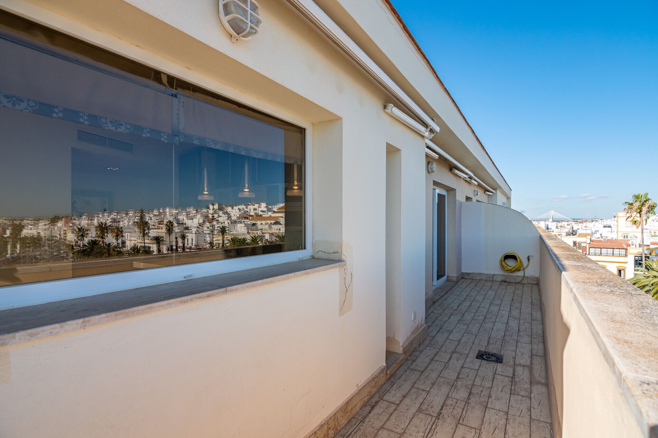 Ein schmaler Balkon mit Blick auf eine Stadtansicht, ein Fenster mit Ausblick auf ein hohes Gebäude und ein Schlauch auf dem Boden.
