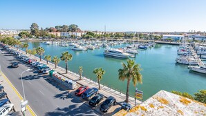 Un puerto deportivo con numerosas embarcaciones amarradas, una zona de estacionamiento con coches y vistas claras de los edificios circundantes.